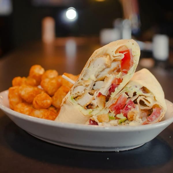 Chicken wrap with diced tomatoes and lettuce, served with a side of crispy tater tots.