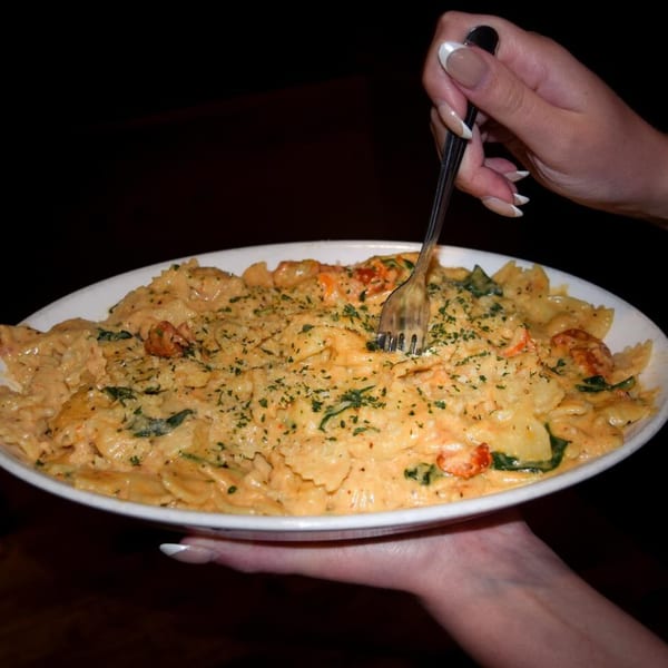 Hands holding a white plate of creamy pasta with shrimp, spinach, and parsley, being forked.
