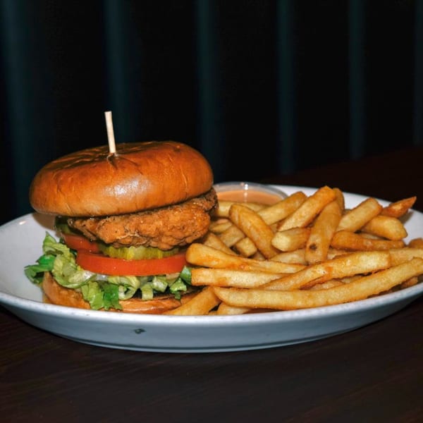 A crispy chicken sandwich with lettuce, tomato, and pickles, served with a side of golden fries.