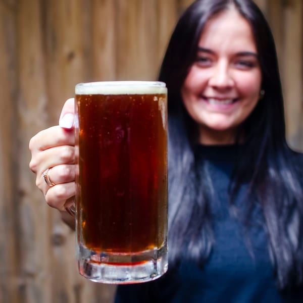 Smiling woman holding a large mug of dark beer with a frothy head at Red Creek Bar & Grill.