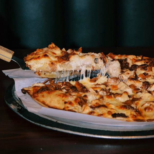 A slice of Red Creek Bar & Grill's cheesy pizza with chicken and bacon being lifted, stretching cheese.