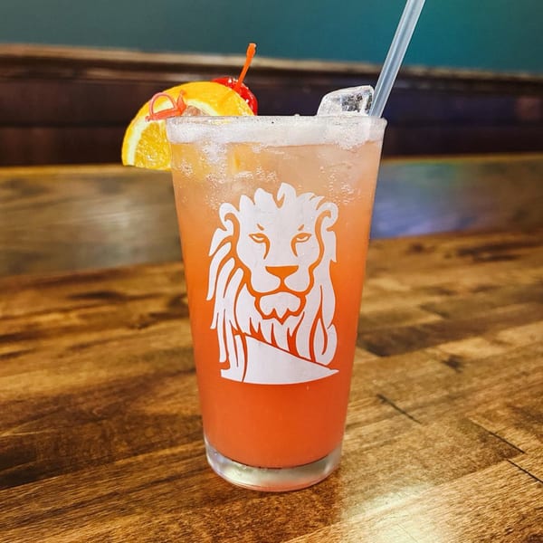 A Red Creek Bar & Grill cocktail with a lion logo, garnished with orange and cherry.