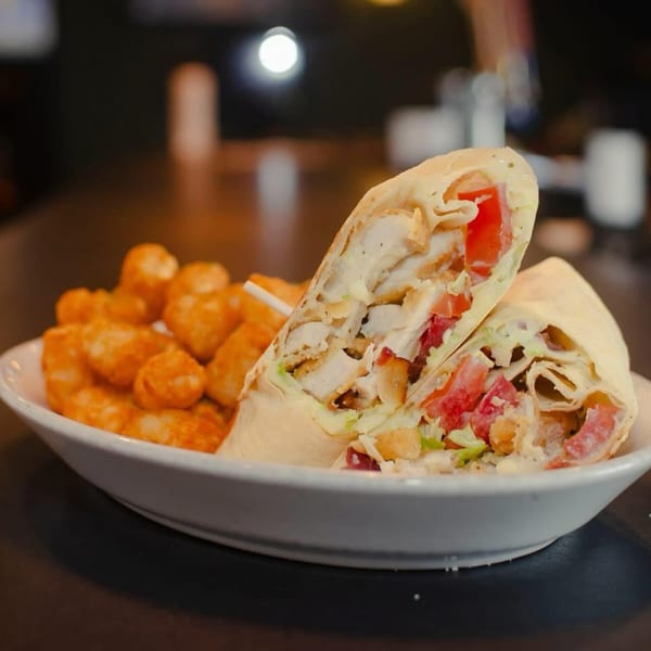 Chicken wrap with tomatoes and lettuce, served with a side of crispy tater tots.
