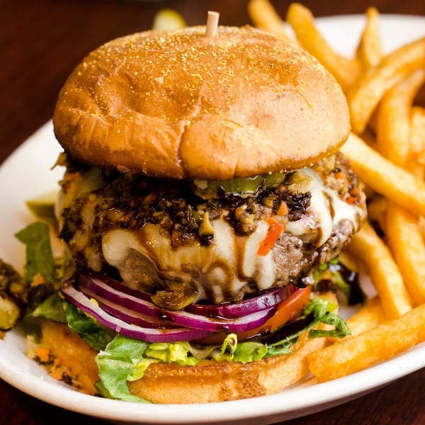 A gourmet burger with melted cheese, red onions, lettuce, and a side of golden fries.