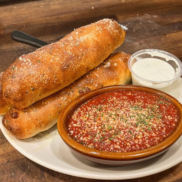 Three golden-brown breadsticks with parmesan cheese and herbs, served with marinara and ranch dipping sauces.