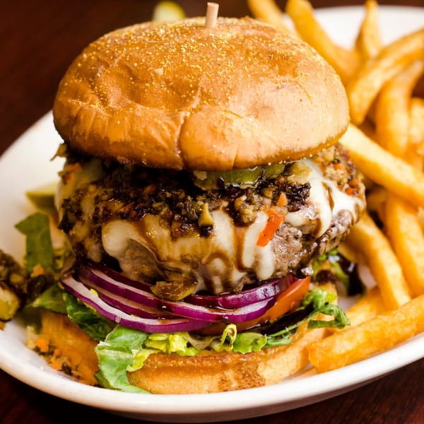 A Red Creek Bar & Grill burger with melted cheese, onions, lettuce, and fries on a white plate.