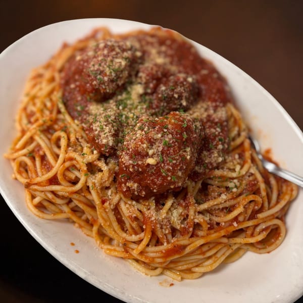 Spaghetti and meatballs with red sauce, parmesan cheese, and parsley in a white bowl.